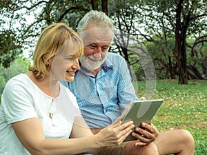 Happy Senior couple sitting on the green grass and enjoying using laptop for online entertainment in the park, Happy life and