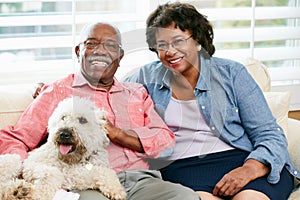 Happy Senior Couple Sitting On Sofa With Dog