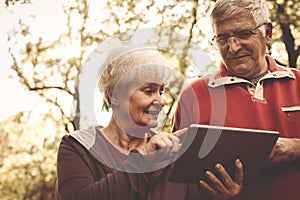 Happy senior couple standing in park and using iPod.