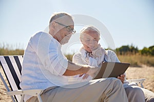 Happy senior couple with tablet pc on summer beach