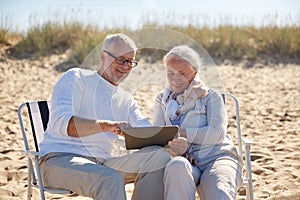 Happy senior couple with tablet pc on summer beach