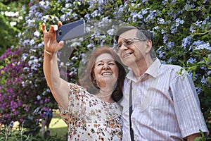 Happy senior couple taking a self portrait in a garden, surrounded by flowers