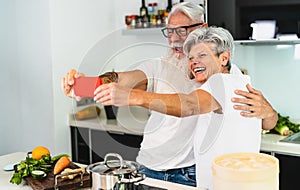 Happy senior couple taking selfie while cooking together at home - Elderly people having fun preparing health lunch in kitchen