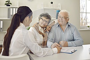 Happy senior couple talking to family practitioner sitting at table at doctor's office