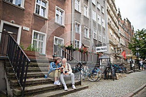 Happy senior couple tourists sitting on stairs and having take away coffee outdoors in town