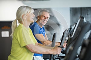 Happy senior couple training on stair stepper at gym