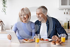 Happy senior couple using digital tablet while having breakfast