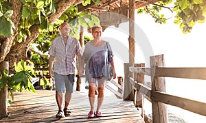 Happy senior couple walking holding hand at Koh Phangan beach promenade - Active elderly and travel lifestyle concept