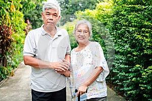 Happy senior couple walking together in the garden. Old elderly using a walking stick to help walk balance. Concept of  Love and