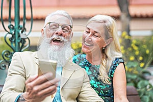 Happy senior couple watching on mobile smart phone and laughing together - Mature fashion people having fun with new technology