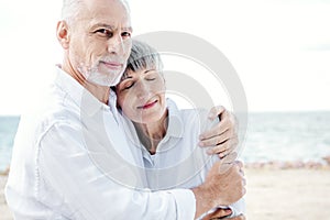 happy senior couple in white shirts embracing at beach.