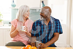 Happy senior diverse couple drinking coffee in kitchen