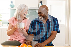 Happy senior diverse couple drinking coffee in kitchen