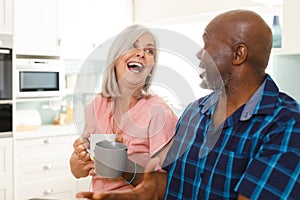 Happy senior diverse couple drinking coffee in kitchen