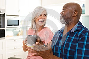 Happy senior diverse couple drinking coffee in kitchen