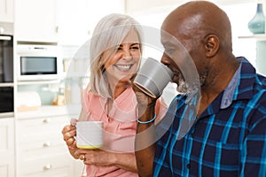 Happy senior diverse couple drinking coffee in kitchen