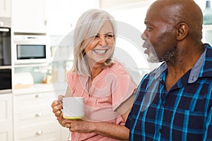 Happy senior diverse couple drinking coffee in kitchen