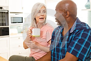 Happy senior diverse couple drinking coffee in kitchen