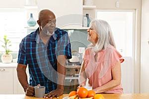 Happy senior diverse couple drinking coffee in kitchen