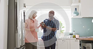 Happy senior diverse couple drinking coffee in kitchen