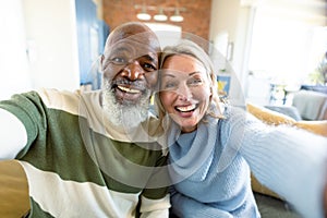 Happy senior diverse couple in living room sitting on sofa, making video call