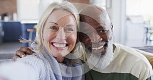 Happy senior diverse couple in living room sitting on sofa, making video call