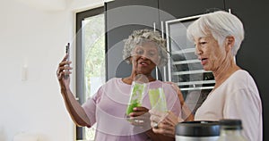 Happy senior diverse women drinking healthy drink in kitchen at retirement home