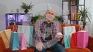 Happy senior elderly grandfather man celebrating birthday party, makes wish blowing burning candle