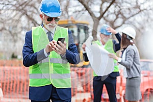 Happy senior engineer or businessman using his smart phone while inspecting a construction site