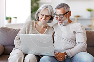 Happy senior family couple watching comedy or funny video on laptop while spending free time at home