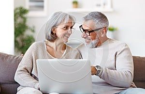 Happy senior family couple watching comedy or funny video on laptop while spending free time at home