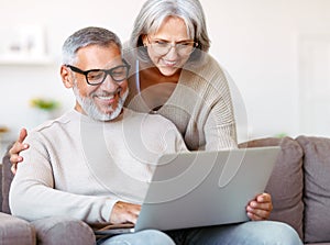 Happy senior family couple watching comedy or funny video on laptop while spending free time at home