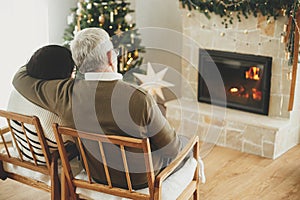 Happy senior family enjoying cozy fireplace. Happy holidays! Beautiful elderly couple hugging and relaxing in stylish christmas