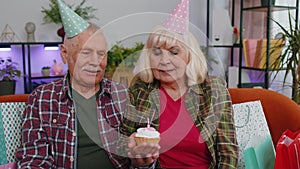 Happy senior family man woman celebrating birthday anniversary hold cupcake makes wish at home