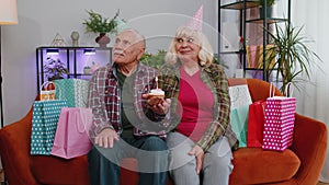 Happy senior family man woman celebrating birthday anniversary hold cupcake makes wish at home