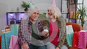 Happy senior family man woman celebrating birthday anniversary hold cupcake makes wish at home