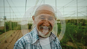 Happy senior farmer smiling at the camera while working inside greenhouse
