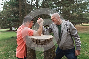 Happy senior father with his adult son with Down syndrome arm wrestling in park.