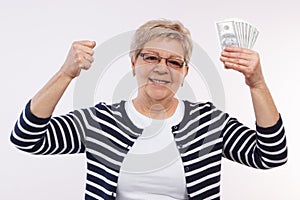 Happy senior female holding currencies dollar and clenching her fist, concept of financial security in old age