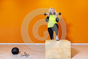 Happy senior fit woman doing weight lifting workout exercise standing at the gym  on orange background. mature people