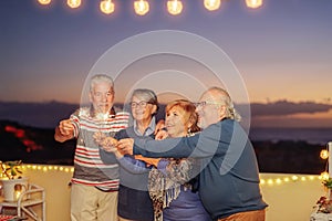 Happy senior friends celebrating birthday with sparklers stars outdoor - Older people having  fun in terrace in the summer nights