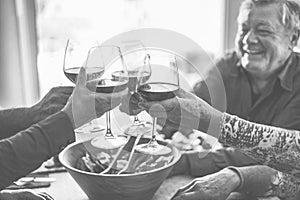 Happy senior friends having fun cheering with red wine - Mature people eating at dinner and laughing together - Black and white