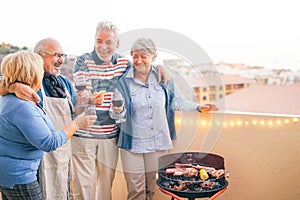 Happy senior friends having fun drinking red wine at barbecue dinner in terrace - Mature people dining and laughing together