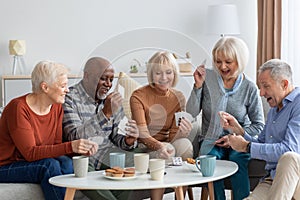 Happy senior friends playing cards while chilling together at home