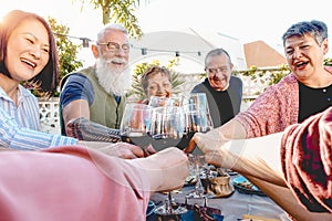 Happy senior friends toasting with red wine glasses at dinner on patio - Mature people having fun dining together outside