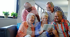 Happy senior friends using digital tablet on sofa