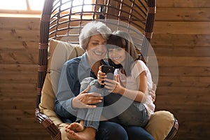 Happy senior grandmother and granddaughter use smartphone laughing