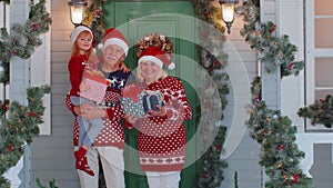 Happy senior grandparents with granddaughter holding many gift boxes near Christmas house, celebrate