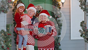 Happy senior grandparents with granddaughter holding many gift boxes near Christmas house, celebrate