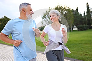 Happy senior husband and wife in sportive outfits running outdoors in city park